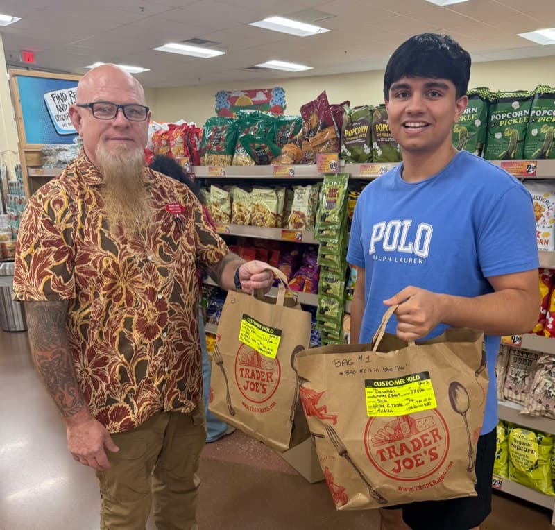 Sid Sharma and a Trader Joe's crew member holding two bags tagged as Waste2Taste donations