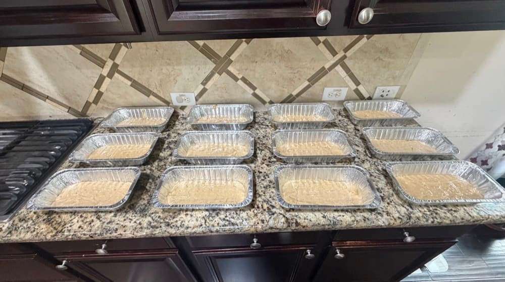Twelve loaf pans of banana bread batter lined up on a kitchen counter