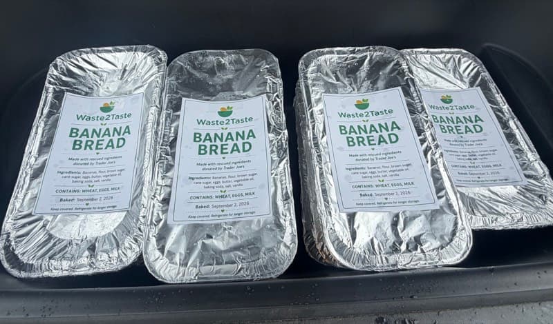 Four foil pans of Waste2Taste banana bread with ingredient labels packed in a car trunk