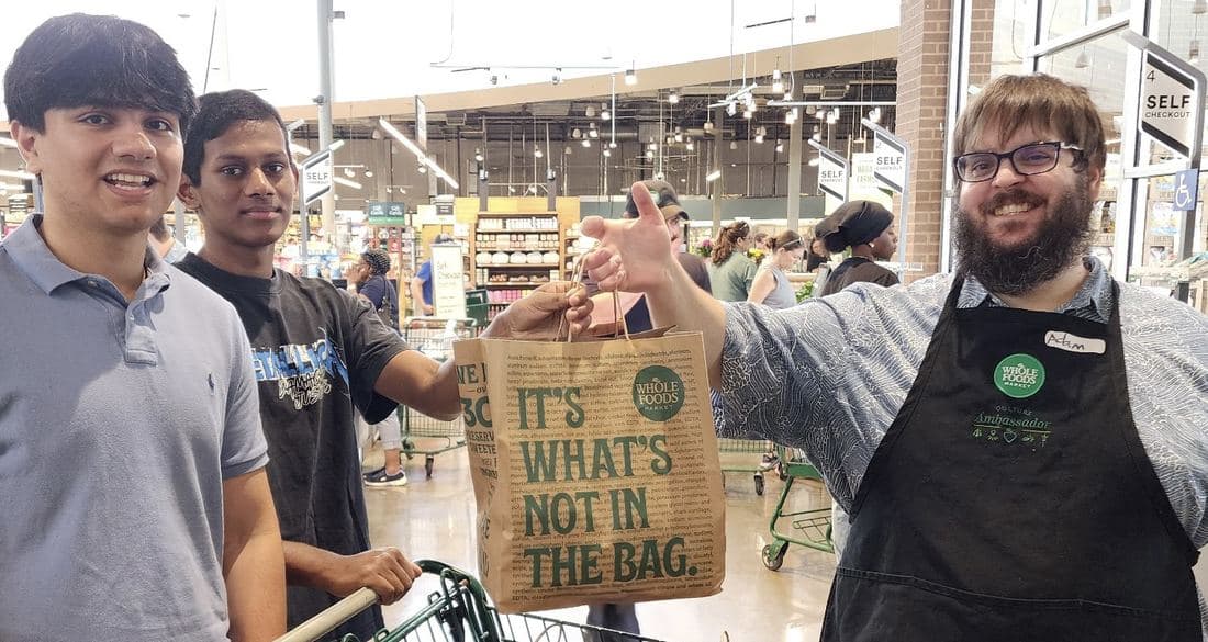 Sid Sharma and a volunteer taking a Whole Foods bag from a Whole Foods team member in the store